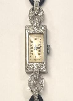 Ladies diamond and platinum hand wound dress watch c1930 on a black cordette strap with silvered buckle. Silvered dial with black Arabic hours and minute track and black hands. Swiss FHF jewelled lever movement with split bi-metallic balance and case back stamped 'PLATINO'.