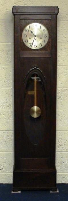 German dark oak cased, grandfather longcase clock. Plain straight line case with moulded swag surrounds to the visible pendulum window. Silvered face with black painted arabic hour markers and black steel hands. 8 day Westminster chiming movement circa 1930, with a lever control to turn off the quarters chime. The back plate is stamped D.R.G.M 989568. (D.R.G.M. signifies "Deutsche Reich Gebraumeister" and is a design or use patent somewhat similar a "Registered" mark.)  Case dimensions - height 71", width 17", depth 8".