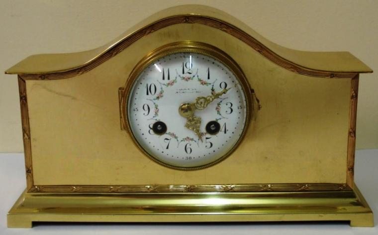 French 8 day gilt brass cased mantel clock. Gilt bezel with convex chamfered glass over white enamel dial with black arabic hour markers and ornate gold coloured hands and pretty floral  swag decoration.  Brass drum movement circa 1900, with platform lever escapement, spring driven and striking an a gong.