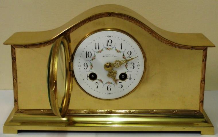 French 8 day gilt brass cased mantel clock. Gilt bezel with convex chamfered glass over white enamel dial with black arabic hour markers and ornate gold coloured hands and pretty floral  swag decoration.  Brass drum movement circa 1900, with platform lever escapement, spring driven and striking an a gong.