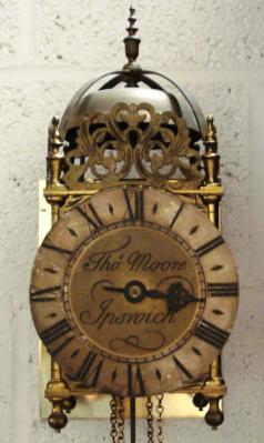 English reproduction 30 hour lantern clock signed to the dial 'Thos. Moore, Ipswich'. Brass and steel case with silvered chapter ring with black roman hours and blued steel hour hand. The good quality brass 30 hour movement has a single iron weight and brass and steel pendulum and strikes the hours on a bell.  Dimensions: Height - 15.5", Width - 6.5", Depth 7.5".