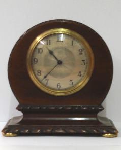 French 8 day mantel timepiece circa 1920 with round top dark mahogany case with carved plinth decoration and gilt bun feet. Gilt brass bezel with convex glass over a silvered dial with engine turned centre and black arabic hours and black steel hands. Brass drum movement with contemporary cylinder escapement platform, and stamped 'Made in France' with a captive winding key.  Dimensions: Height - 7", width - 6.5", depth - 3.75".