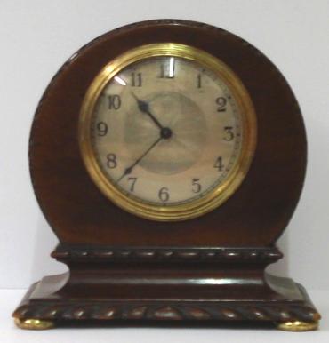 French 8 day mantel timepiece circa 1920 with round top dark mahogany case with carved plinth decoration and gilt bun feet. Gilt brass bezel with convex glass over a silvered dial with engine turned centre and black arabic hours and black steel hands. Brass drum movement with contemporary cylinder escapement platform, and stamped 'Made in France' with a captive winding key.