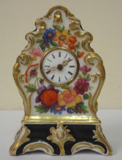 Good quality porcelain cased bedside or mantel clock with applied gilding and enamel flower decoration throughout. White enamel dial with slight damage, black roman hours and ornate gilt metal hands. Miniature brass spring driven late 19th century 8 day movement, maker unknown, with gilt pendulum.  Dimensions: Height - 3.5", width - 2.25", depth - 1.5".