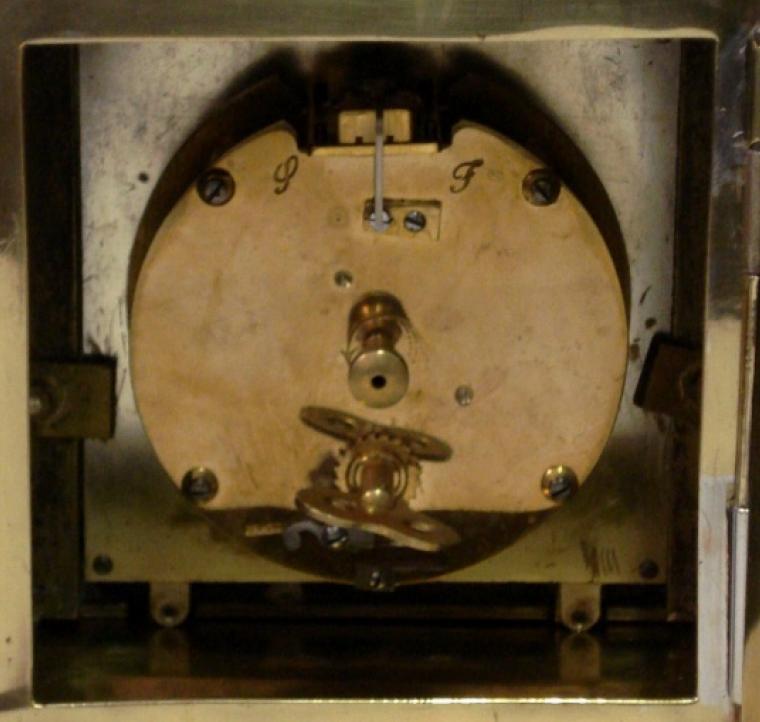 French 8 day brass cased mantel clock timepiece circa 1910. Dome topped case with decorative brass side pillars and ornate rear door hinge. Cutout brass front plate with flat glass over silvered dial plate with black roman hours and ornate black steel hands. Circular French brass drum movement, maker unknown. with lever escapement and captive winding key.