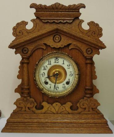 American 8 day oak cased 'Vernon' mantel clock circa 1890, by the Ansonia Clock Co. Highly carved and decorated case with half turned pillars and applied mouldings. Gilt brass bezel with flat chamfered glass over ivorine chapter ring with gilt brass centre. Black gothic hours and ornate black steel hands and slow / fast adjuster at 12 o'clock. Spring driven, gong striking skeletonised brass movement with original pendulum, and stamped 'Ansonia Clock Co.' and 'Patented - June 18, 1882'.