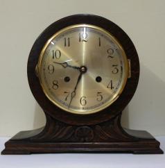 8 day dark stained oak and pine cased mantel clock circa 1920. Balloon shaped case with applied decorative moulding. Circular gilt bezel with convex glass, silvered dial with black arabic hours and black steel hands and strike / silent selection at 3 o/c. Square brass pendulum regulated, spring driven, gong striking movement, maker unknown.  Dimensions: Height - 9.5", width - 11", depth - 6".