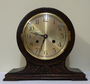 8 day dark stained oak and pine cased mantel clock circa 1920. Balloon shaped case with applied decorative moulding. Circular gilt bezel with convex glass, silvered dial with black arabic hours and black steel hands and strike / silent selection at 3 o/c. Square brass pendulum regulated, spring driven, gong striking movement, maker unknown.