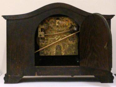 8 day dark stained oak cased Westminster chime mantel clock circa 1920. Oblong case with wave top and integral barley twist columns and applied decorative mouldings. Circular brass bezel with convex glass over a silvered dial with black arabic hours and blued steel hands. Square brass spring driven, rod striking movement with decorative wriggle work back plate, stamped #2113, and a vertically mounted French lever escapement.