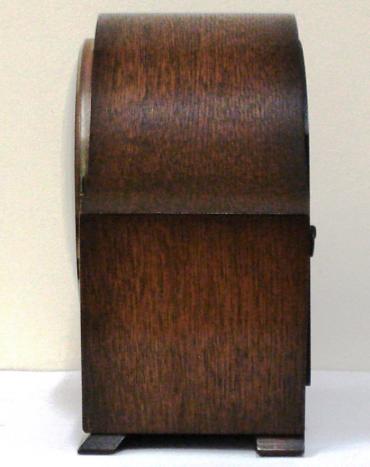 English 8 day oak veneer cased mantel clock circa 1950 by Smiths. Angular round topped case with delicate side moulding and a circular brass bezel with convex glass over an ivory coloured chapter ring. Gilt arabic hours and fretwork hands and Chime / Silent control at 9 o/c. Good quality pendulum regulated, spring driven, rod striking brass movement with decorative engine turning and stamped '-Smiths-, Made in Great Britain, Smiths English Clocks Ltd.'.