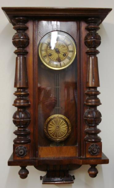 Clock for sale for restoration:- Vienna Regulator style walnut and pine cased gong striking wall clock by Kienzle. Flat top pediment full length door with fluted and turned side columns, original glass over ivory coloured dial with black roman hours and ornate blued steel hands. Standard brass spring driven pendulum regulated 8 day movement circa 1890 with faux gridiron and sunburst pendulum boss. Back plate has the Kienzle touch mark and is stamped D.R.Patent. Lacks original crest and finials and has discolouration to dial and pendulum suspension spring is broken.