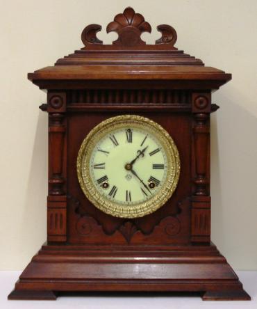 American Ansonia Clock Company 'Sharon' 8 day mahogany veneer pine cased gong strike mantel clock circa 1890. Decorative architectural case with carved and applied moulding and ornate gilt bezel with flat, chamfered glass over an ivory coloured dial with black roman hours and blued steel hands with a slow / fast adjuster at 12 o/c. Good quality brass, spring powered, pendulum driven movement stamped for the Ansonia Clock Co. and displaying a patent date of June 18, 1882.