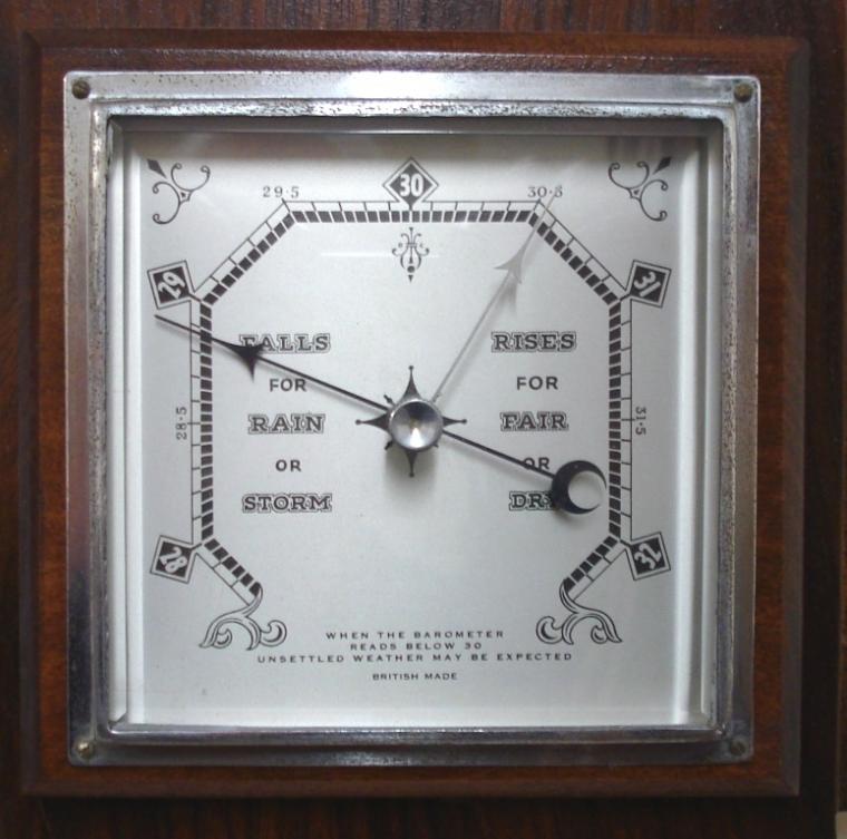 British dark walnut solid wood aneroid barometer circa 1920. Square chromed bezel with flat chamfered glass over a silvered dial with black painted pressure index, blued steel pressure indicator and silvered history pointer. Separate red alcohol Fahrenheit and Centigrade thermometer.  Dimensions: - Height 20", width 7.5", depth 2.5".
