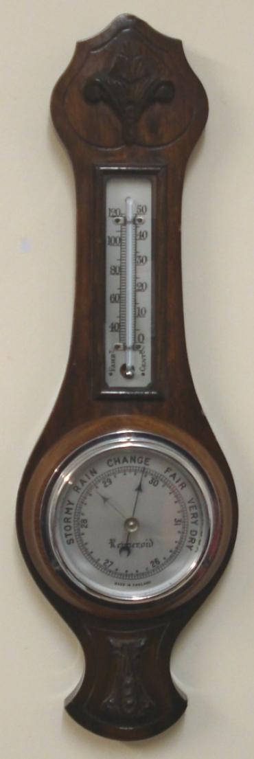 English aneroid barometer in a dark stained oak solid wood carved and moulded case by Renneroid circa 1930. Circular chromed bezel with chamfered glass over a silvered dial with black painted pressure index, blued steel pressure indicator and silvered history pointer. Separate mercury Fahrenheit and Centigrade thermometer.  Dimensions: - Height 18.5", width 5.5", depth 3".