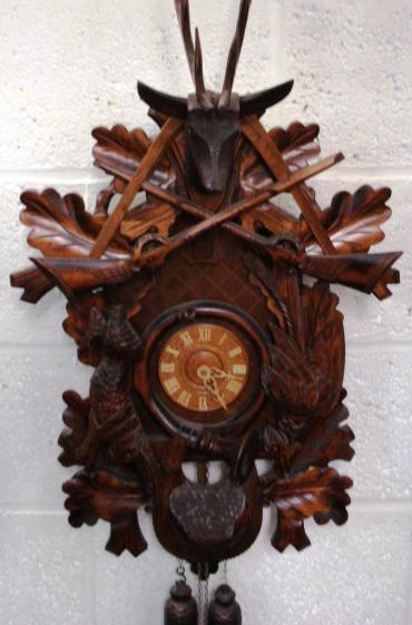 New 2 weight driven 8 day duration cuckoo clock with cuckoo displaying on the hour and half hour and striking on a gong. Elaborate carved case with hunting themes and leaf pendulum, and stag's head finial.