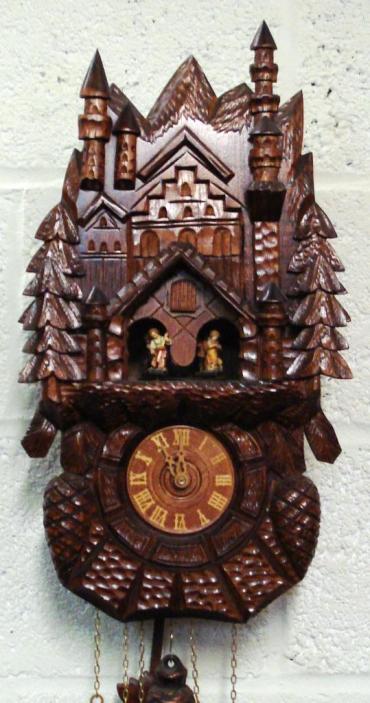 New 3 weight driven 8 day duration cuckoo clock with cuckoo displaying on the hour and half hour and striking on a gong. Decorative carved case with castle themed building, and vine leaf pendulum. The clock features an automaton of dancing figures, and a two tune musical movement.