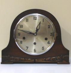 German 8 day oak veneer cased triple chime mantel clock circa 1930. Round topped hump back case with decorative front moulding and a circular chrome bezel with convex glass over a silvered dial. Black arabic hours and fretwork hands and Chime Selection (Westminster, Whittington or St.Michael) / Silent control at 3 o/c. Good quality pendulum regulated, spring driven, rod striking brass movement stamped 'Patent No 421434, Other Patents Pending' and 'Foreign'.  Dimensions: Height - 8.25", width - 10.5", depth - 8".