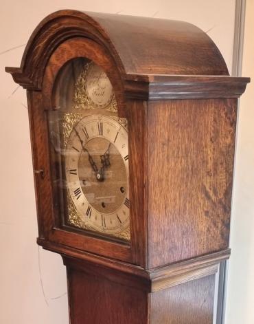 Oak cased 8 day, spring driven, pendulum regulated Westminster chime longcase / grandmother clock by Tempora. Round topped hood with break arch dial with applied brass spandrels and silvered chapter ring. Black Roman hour markers and gothic style black hands with a Chime / Silent selection lever at 3 o'clock. Case dimensions - Height 66", Width 12.5", Depth 9".